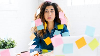 امرأة مغطاة بأوراق صغيرة لتدوين الملاحظات وتستخدم جهاز حاسوب موضوع على طاولة. - Getty Images