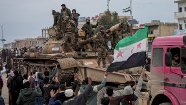 عناصر من الجيش السوري في دير حافر بعد انسحاب قوات سوريا الديمقراطية (قسد)، يقفون على ظهر دبابة ويحملون العلم السوري ذو النجوم الحمراء الثلاثة وحولهم حشد من الناس. - EPA