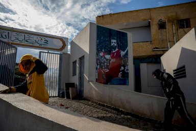 يمرّ مصريون أمام صورة لاعب ليفربول محمد صلاح في مركزه المخصص للشباب والواقع في قرية نجريج المصرية، على بعد نحو 120 كيلومتراً شمال غرب القاهرة، في 10 كانون الأول/ديسمبر 2025