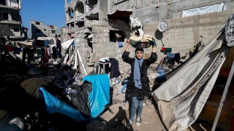 امرأة تحمل خبزاً بجوار المنازل المدمرة في رفح بجنوب قطاع غزة 