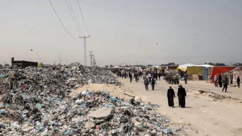 أشخاص يسيرون بالقرب من القمامة المتراكمة في 18 أيار (مايو) 2024 قرب خيام نصبها نازحون فلسطينيون في خان يونس بجنوب قطاع غزة 