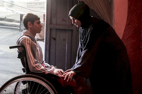 أحد الفتية مبتور الساقين من ضحايا الحرب في غزة يجلس على كرسي متحرك وبمواجهته أمه التي تعتني به بعد أن أصبح معوقا - Getty Images