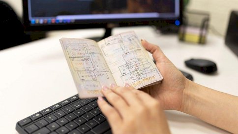 جواز سفر ممتلئ بأختام الدخول والمغادرة بين يدي سيدة ويظهر جهاز حاسوب في خلفية الصورة. - Getty Images