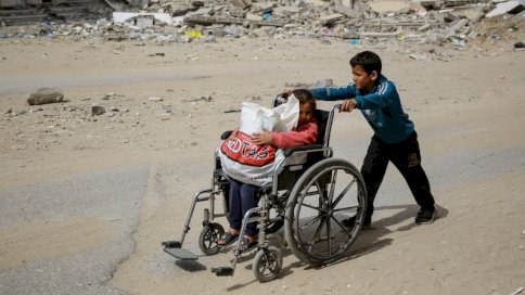 الصراع المستمر بين إسرائيل وحماس: صبي بدفع فتاة صغيرة في كرسي متحرك أمام مبنى مدمر في غزة يوم 28 آذار (مارس) 2024